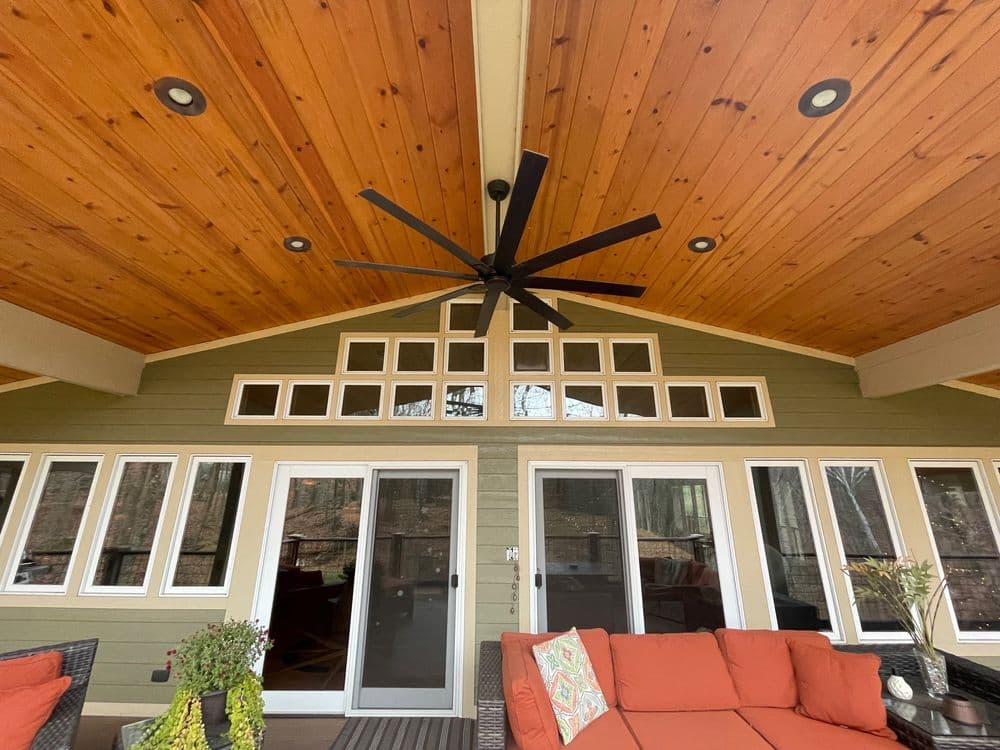Spacious outdoor living area with a wooden ceiling, large fan, and comfortable seating.