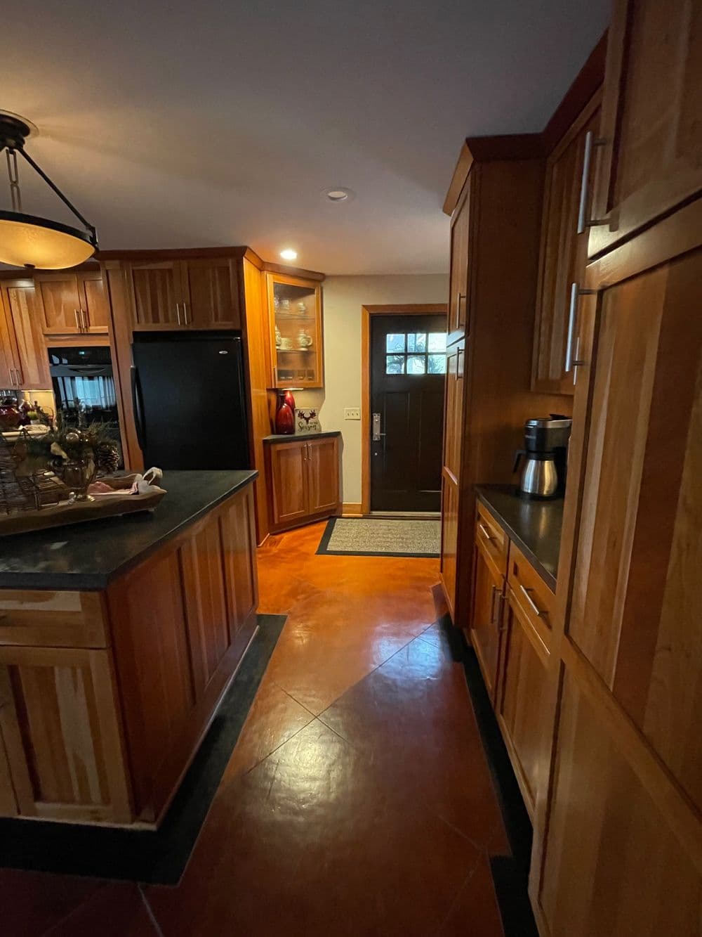 Modern kitchen interior with wooden cabinetry, black appliances, and a doorway to the outside.