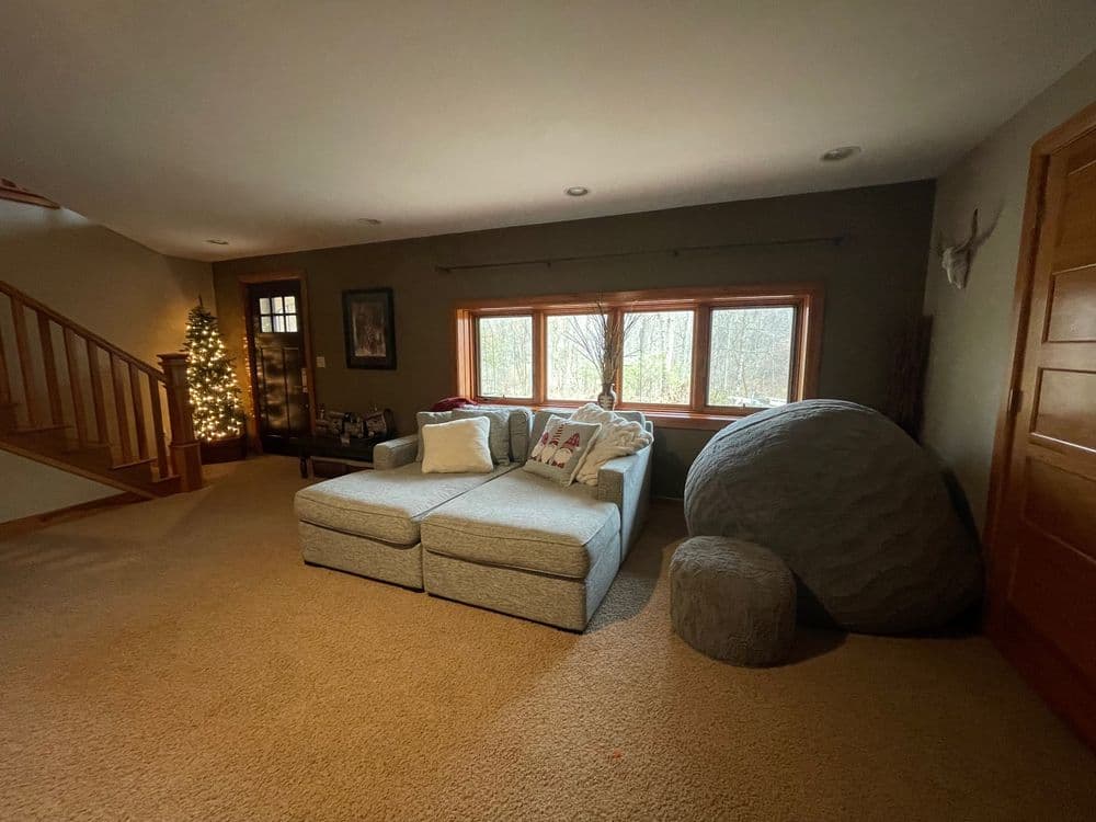 Cozy living room with a sectional sofa, soft carpet, and large windows overlooking nature.