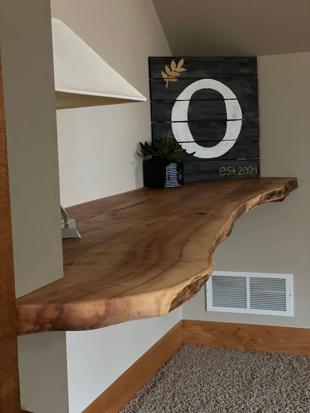 Rustic wooden shelf with a decorative sign and plant against a neutral wall.