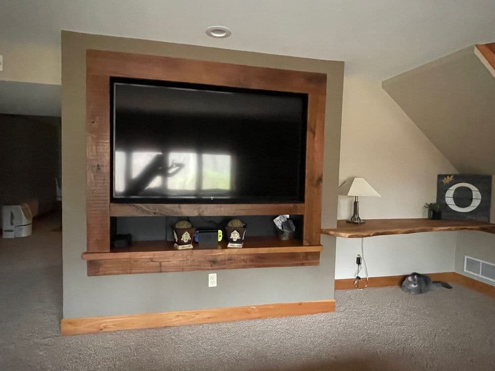 Modern living room with large flat-screen TV framed in wood, cozy atmosphere, and grey cat on carpet.