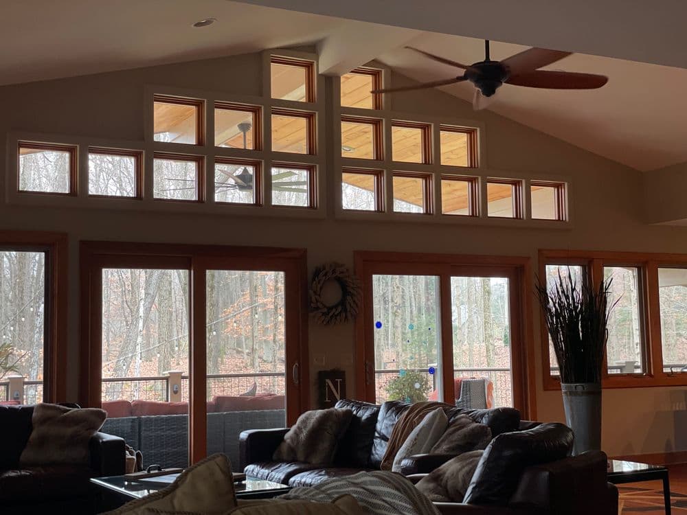 Spacious living room with large windows overlooking a wooded area and rustic furnishings.