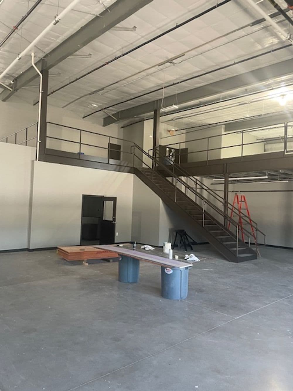 Spacious unfinished interior of a commercial building with a staircase and construction materials.
