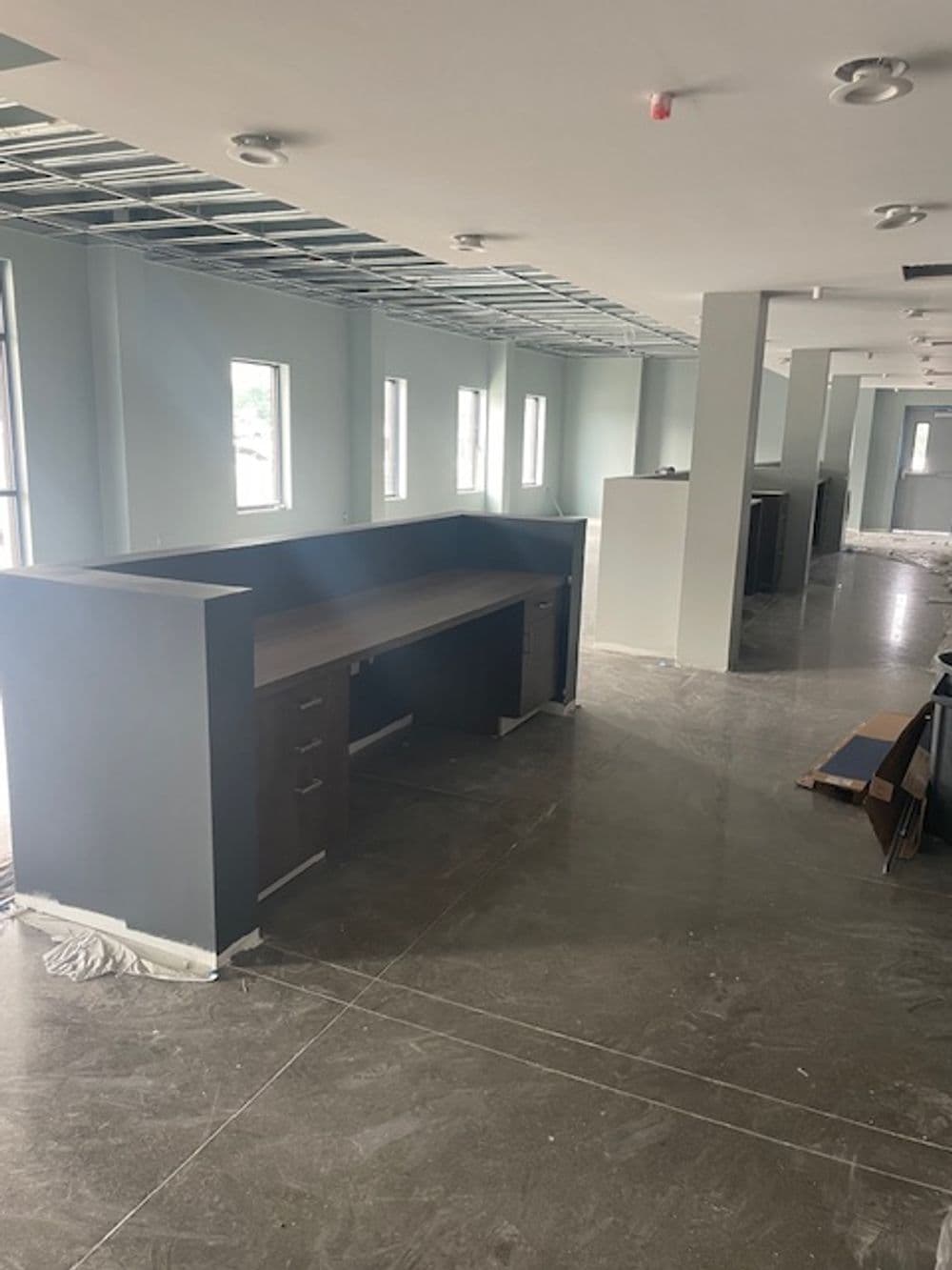 Modern office interior with unfinished walls, large windows, and dark furniture.