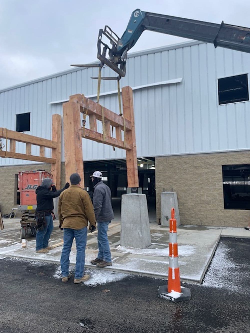 Construction workers installing timber beams with a crane at a building site.