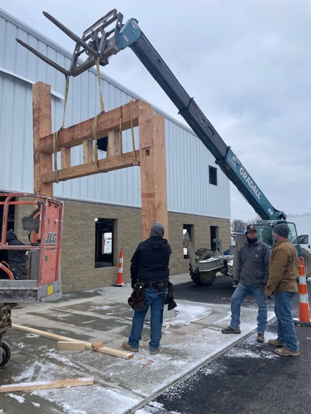 Construction workers using a crane to lift wooden beams at a building site.