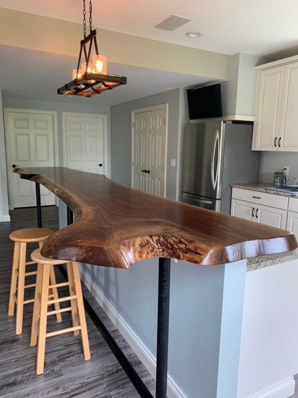 Live edge wood bar top with metal frame and two wooden stools, in a modern kitchen setting.
