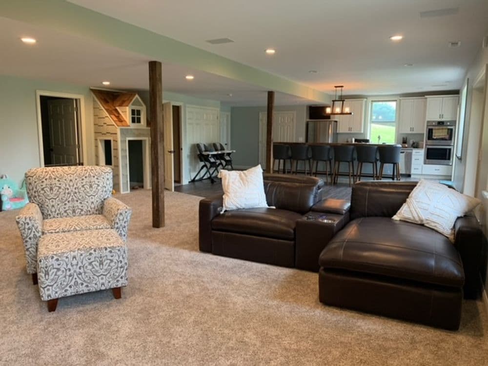 Cozy living room with leather sectional, patterned armchair, and open kitchen in background.