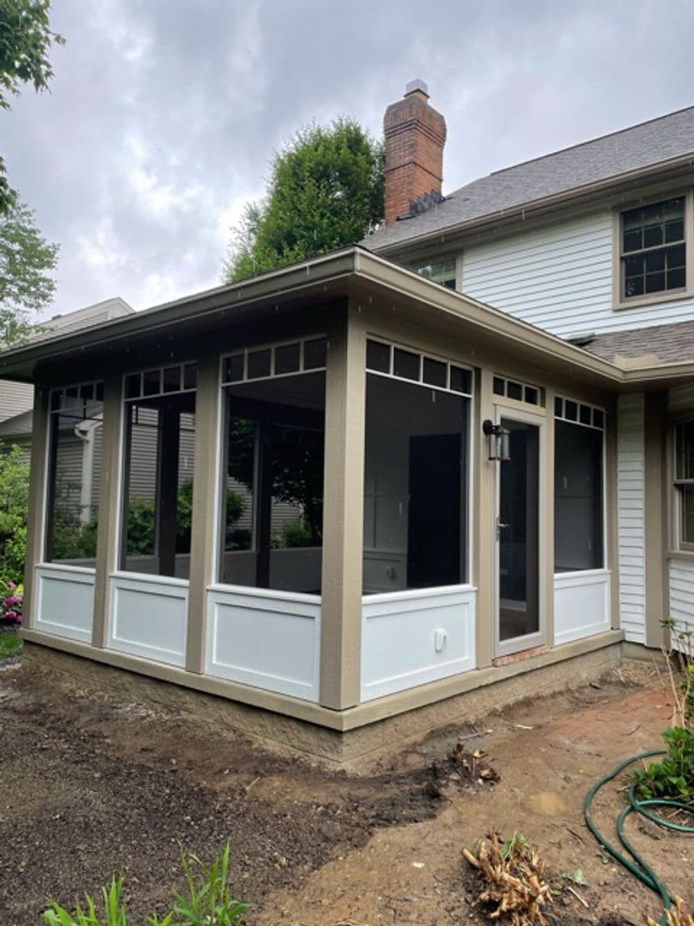 Modern screened-in porch addition with large windows and a chimney on a suburban home.
