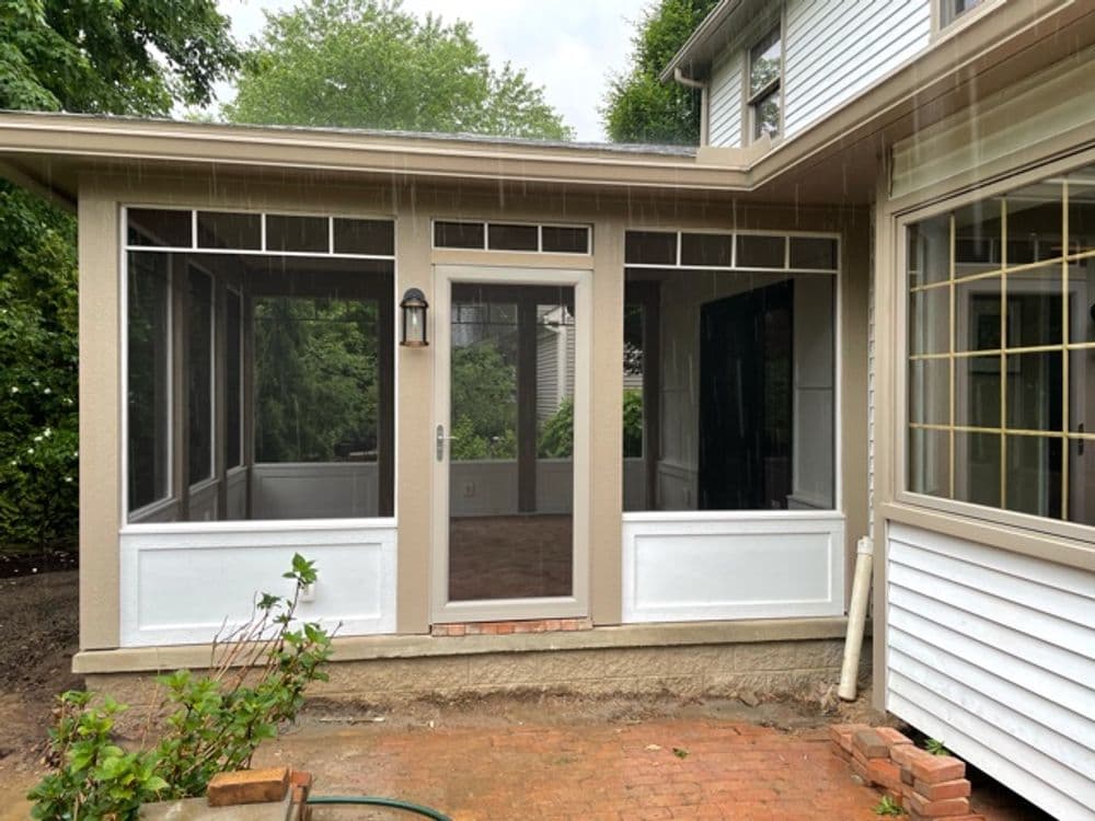 Screened-in porch entry with glass panels and a light fixture, surrounded by greenery.