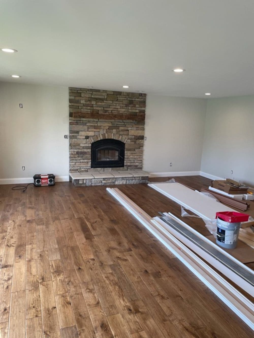 Living room with stone fireplace, wooden flooring, and construction materials scattered around.