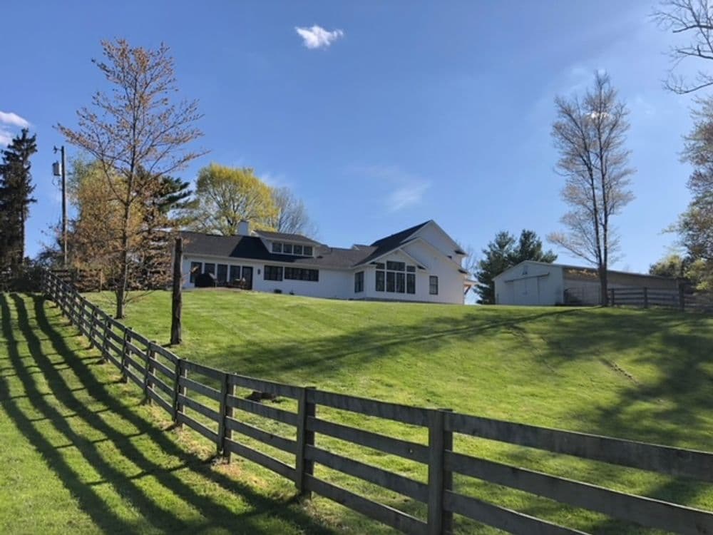 Modern white house with large windows on a grassy hill, surrounded by a wooden fence.